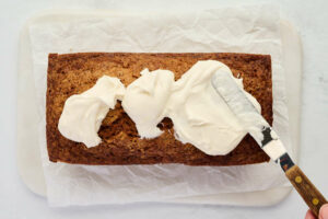 Spreading frosting on top of carrot cake bread.