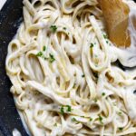 Creamy alfredo sauce coating fettuccini noodles in a sauce pan.