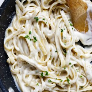 Creamy alfredo sauce coating fettuccini noodles in a sauce pan.