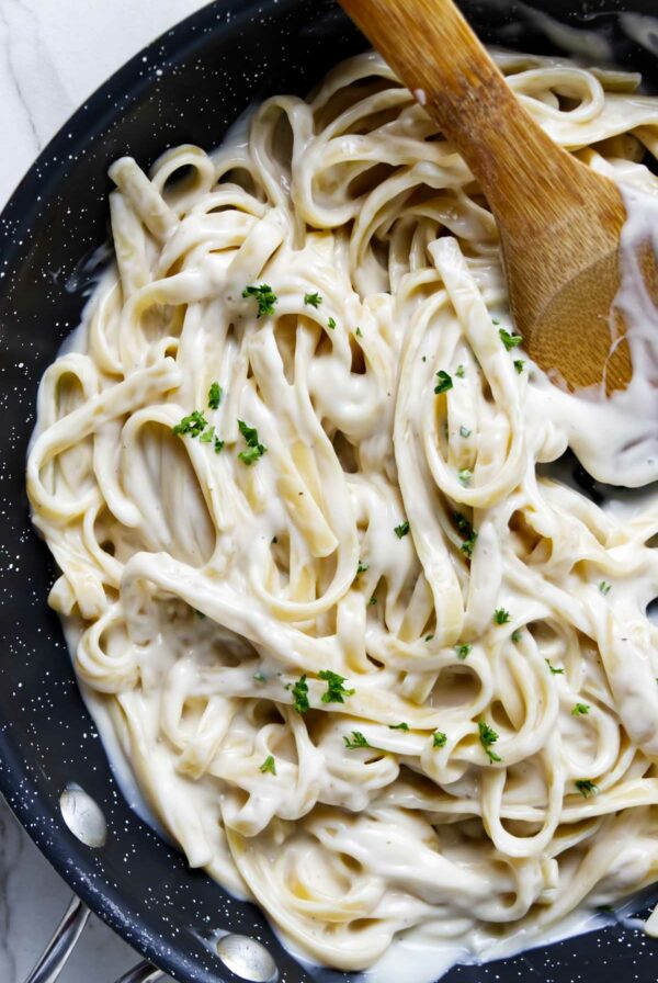 Creamy alfredo sauce coating fettuccini noodles in a sauce pan.