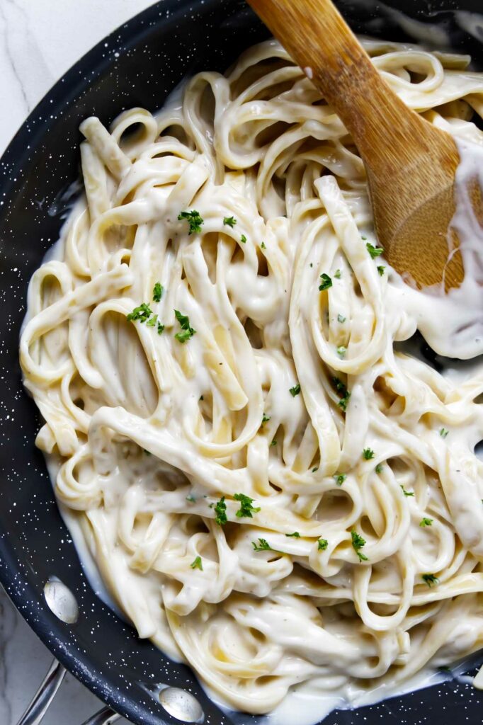 Creamy alfredo sauce coating fettuccini noodles in a sauce pan.