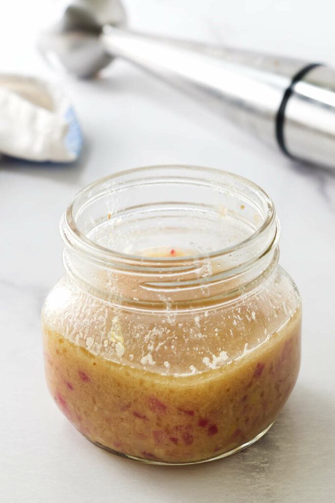 A jar filled with warm bacon dressing in front of a stick blender.