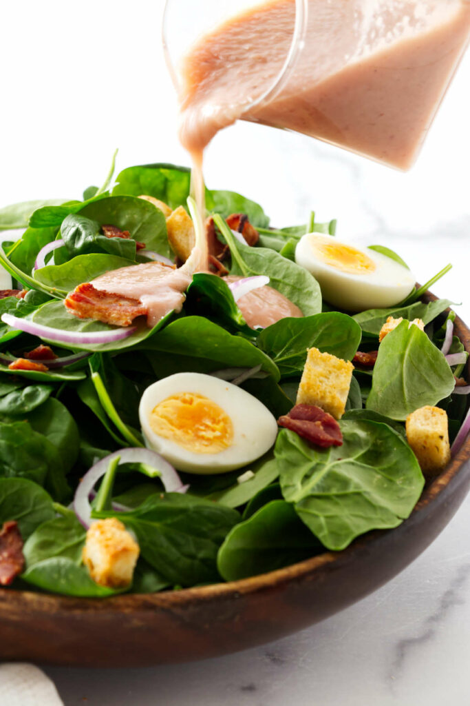 Pouring hot bacon dressing over a spinach salad.