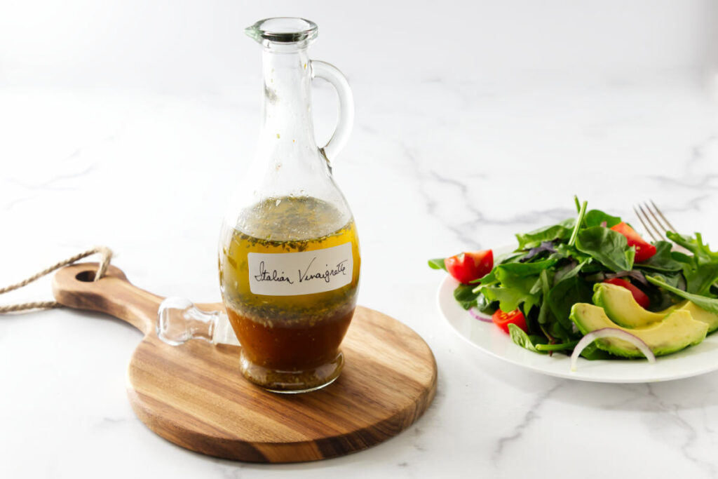 A bottle of vinaigrette dressing next to a plate filled with a green salad.