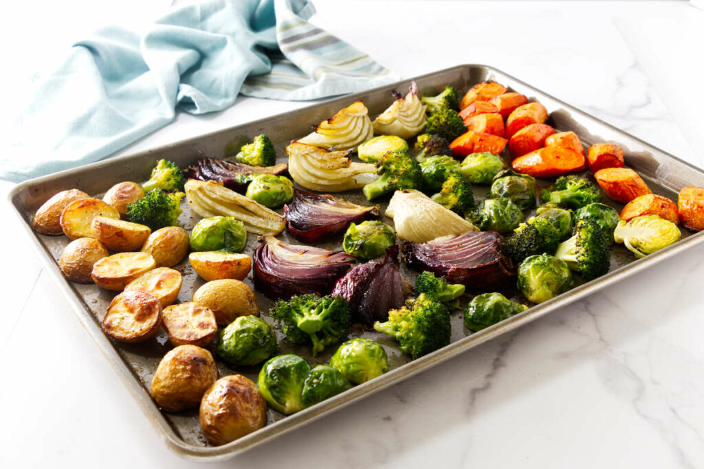 Roasted vegetables on a baking sheet, white surface, blue cloth nearby.