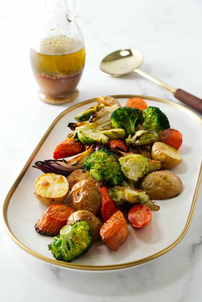 A platter filled with roasted vegetables next to a bottle of Italian dressing.