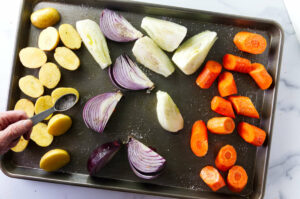 Adding salt to mixed vegetables on a sheet pan.