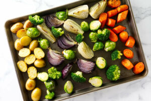 Baking sheet of assorted raw vegetables grouped on a marble surface.