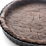 Close-up of chocolate tart crust with fork holes in a black pan.