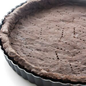 Close-up of chocolate tart crust with fork holes in a black pan.