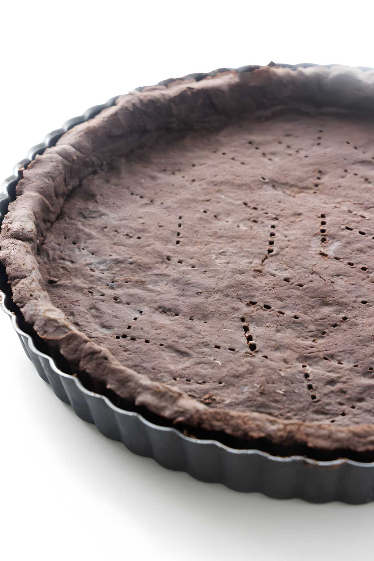 Close-up of chocolate tart crust with fork holes in a black pan.