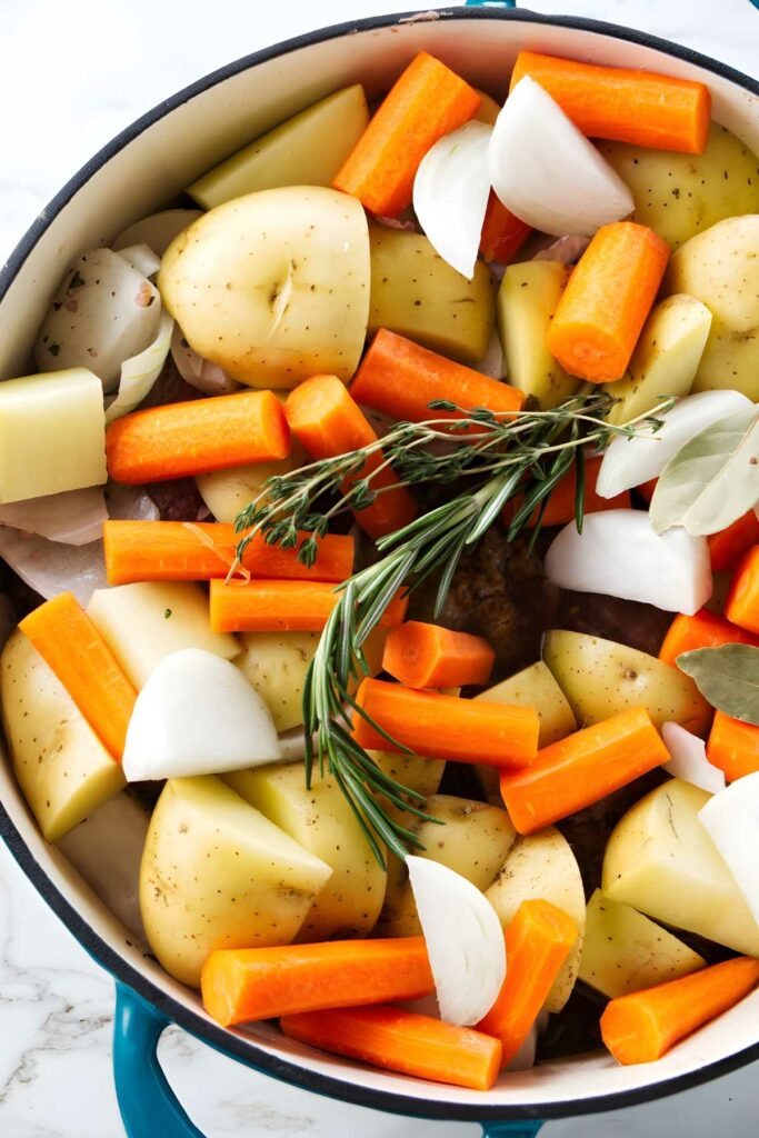 Pot of chopped potatoes, carrots, onions, rosemary and bay leaves ready to cook.