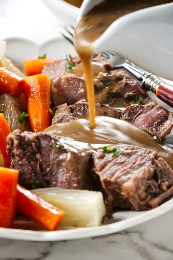 Pot roast with carrots, onions, and gravy on a plate; fork and knife nearby.