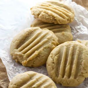Five peanut butter cookies on parchment, one with a bite taken.