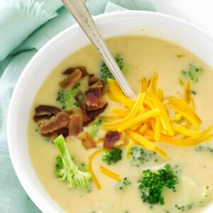 Creamy broccoli soup with cheddar, bacon, and florets in a bowl with spoon.