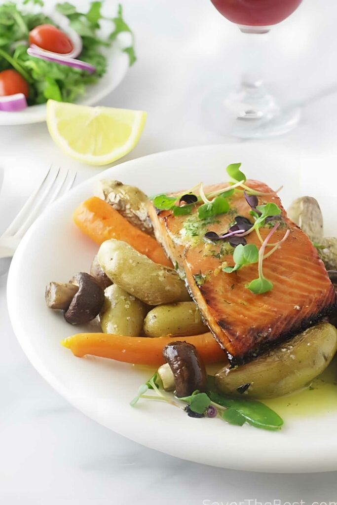 Roasted salmon with dill butter, baby potatoes, carrots, and mushrooms on a plate.