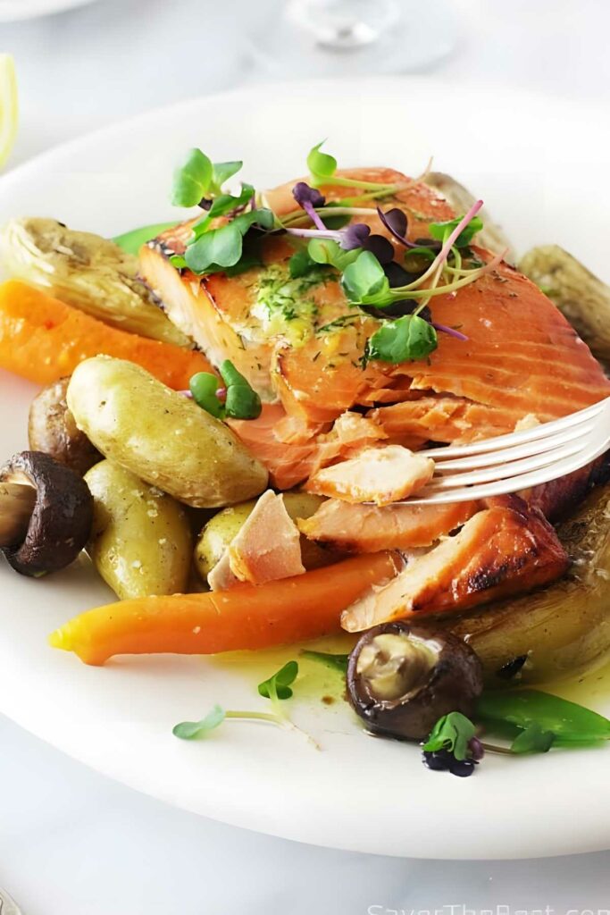 Cooked salmon with microgreens and roasted vegetables, fork flaking the fish.