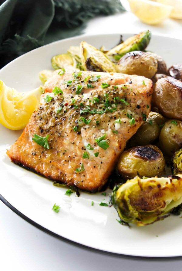 Salmon fillet with herbs, roasted Brussels sprouts, potatoes, and lemon wedge.