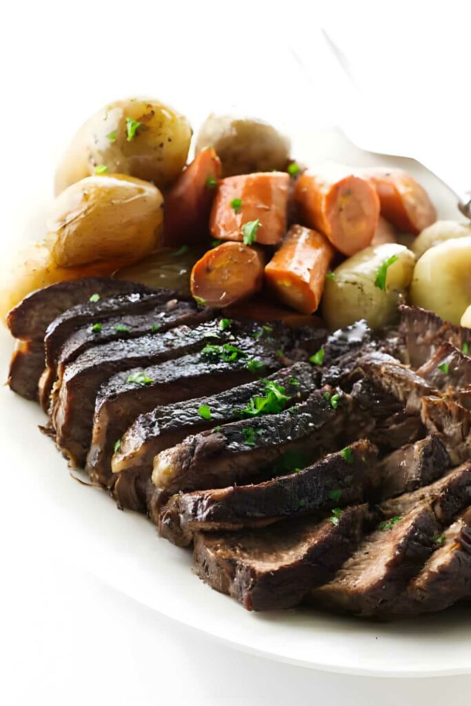 Pot roast slices with parsley, carrots, and potatoes on a white plate.