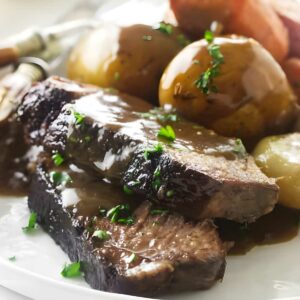 Pot roast slices with gravy, potatoes, and carrots on a white plate.