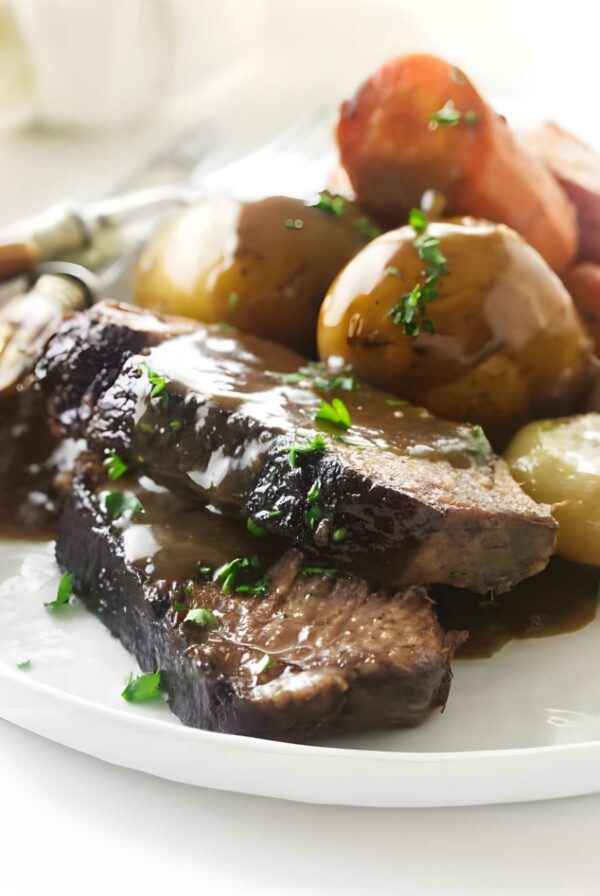 Pot roast slices with gravy, potatoes, and carrots on a white plate.