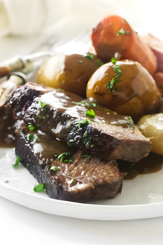 Pot roast slices with gravy, potatoes, and carrots on a white plate.