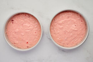 Adding cherry cake batter to cake pans.