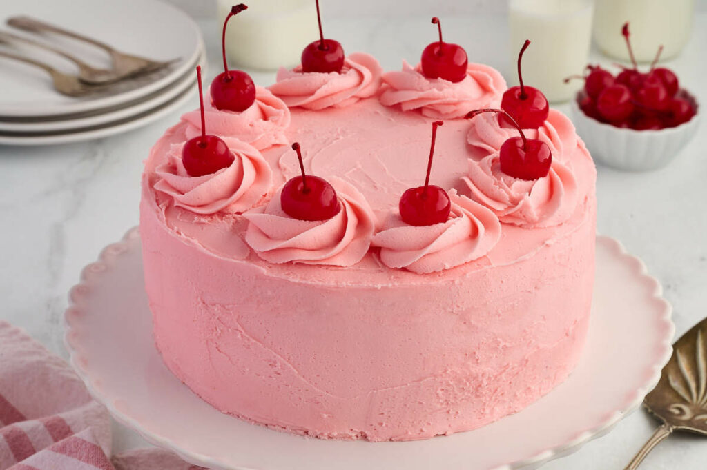 A round cake frosted with pink buttercream and topped with maraschino cherries.