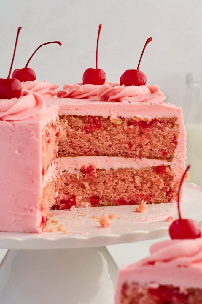 An old fashioned cherry chip cake partially sliced on a cake plate.