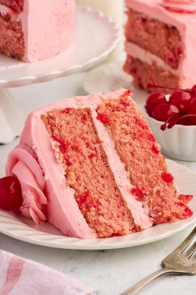 A slice of maraschino cherry cake on a white plate.