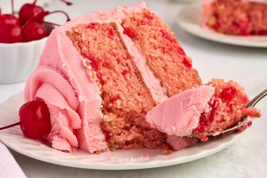 A fork taking a bite from a slice of maraschino cherry chip cake.