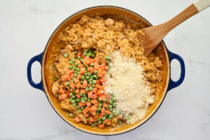 Stirring in veggies and parmesan cheese to the rice and chicken skillet.