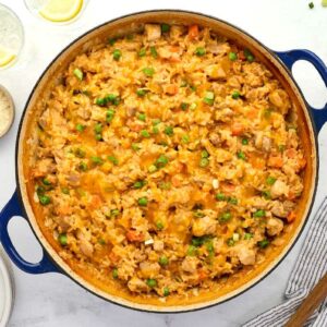 Blue pot of creamy chicken and rice with vegetables, surrounded by cooking tools.
