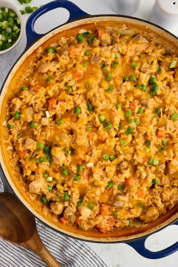 A skillet with baked chicken and rice topped with peas and carrots.
