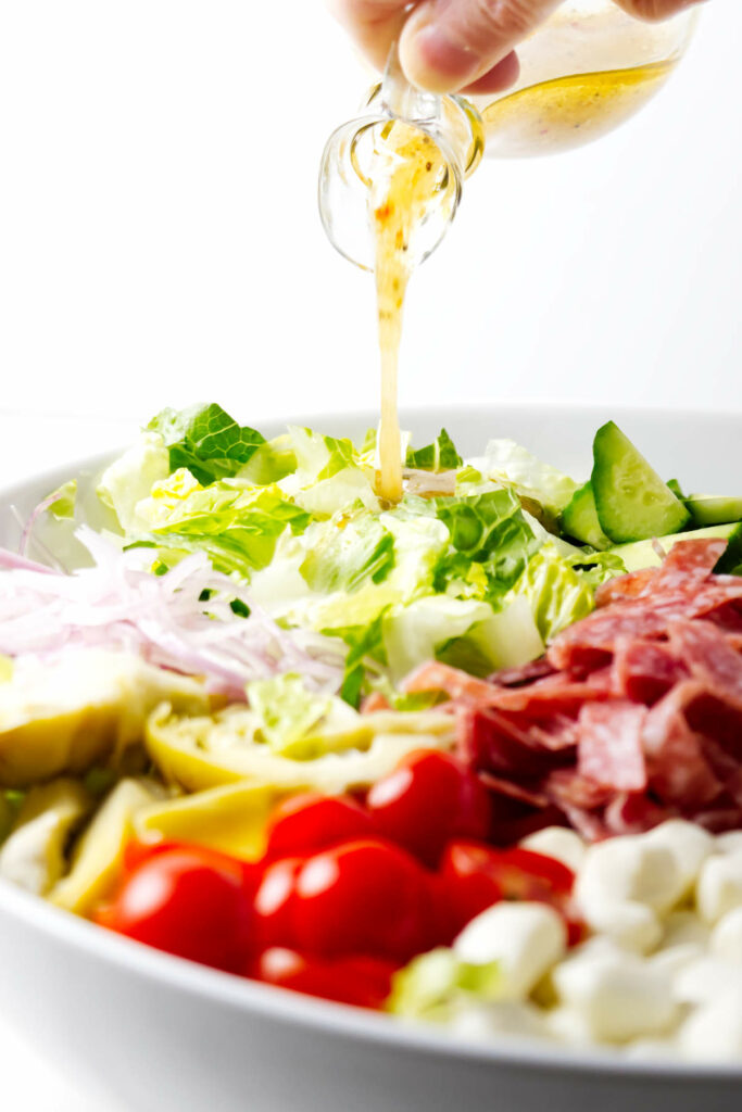 Pouring Italian dressing over a chopped salad.