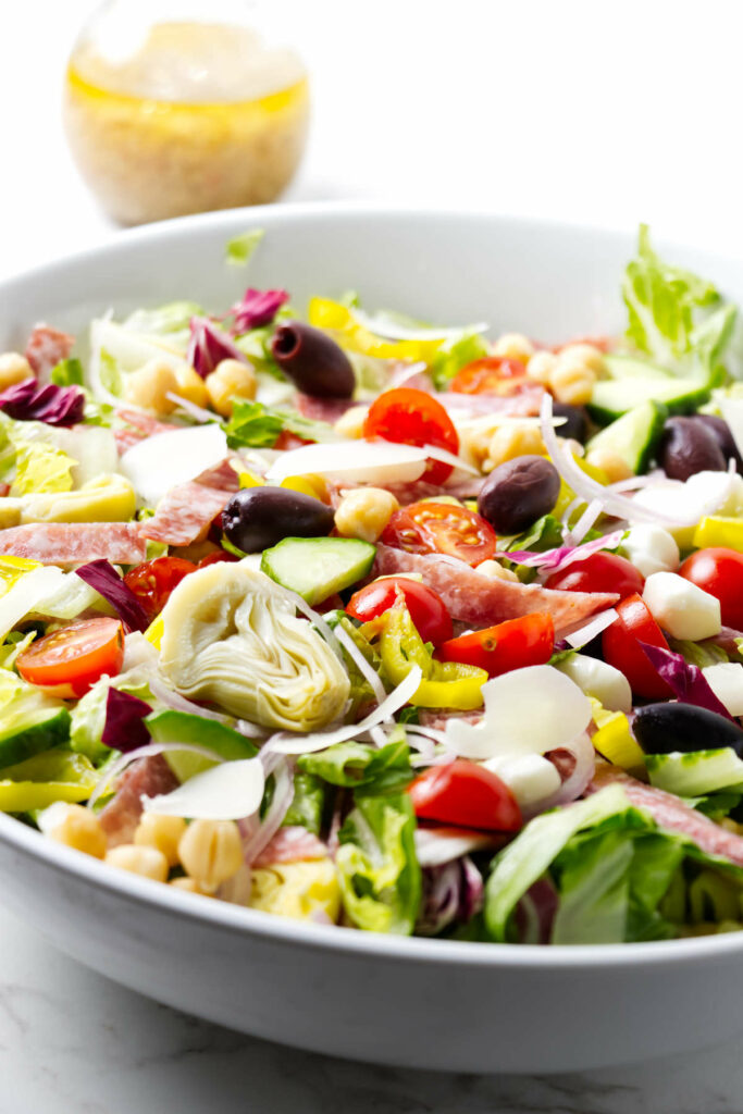 A chopped Italian salad in a large bowl with a bottle of dressing in the background.