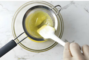 Straining lemon curd through a mesh strainer.