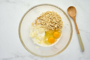 Adding crushed crackers, eggs and milk to a mixing bowl.