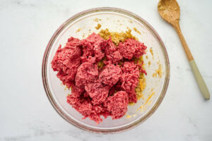 Adding ground beef to the meatloaf mixture.
