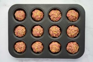 Adding the ground meatloaf mixture to a muffin tin.