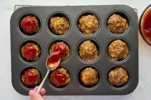 Adding the ketchup glaze to the top of the muffin pan meatloaf.