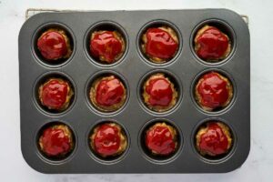 Glazing the top of the mini meatloaves in a muffin pan.