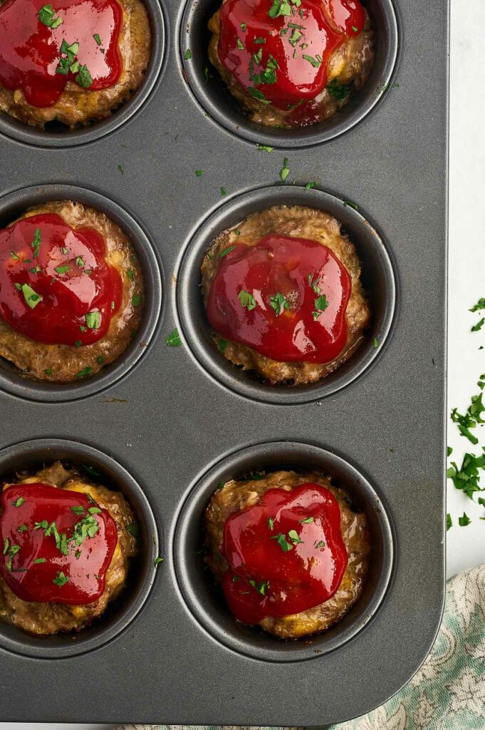 Several mini meatloaves in a muffin tin garnished with parsley.