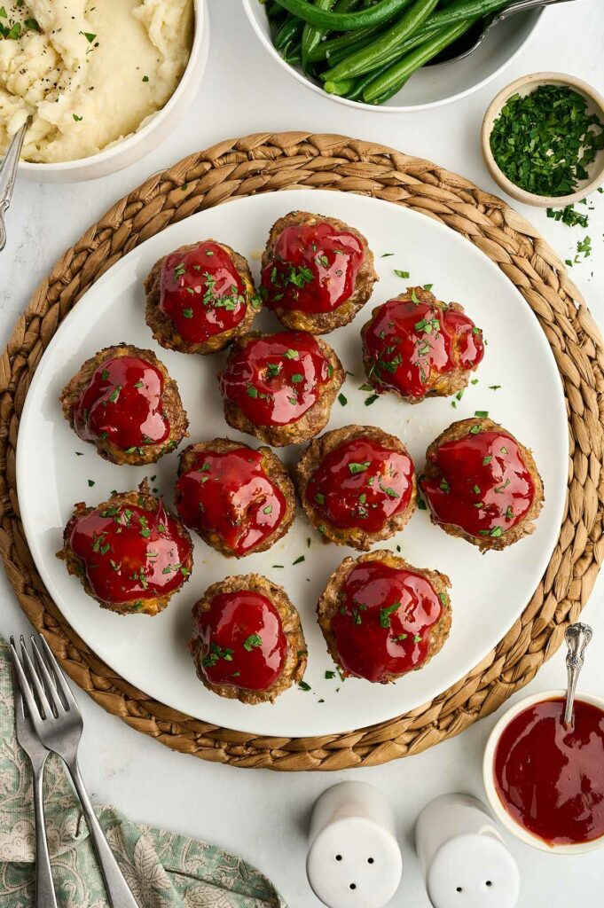 Twelve mini meatloaf muffins on a serving plate next to mashed potatoes.