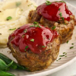 Mini meatloaves with ketchup glaze, mashed potatoes, and green beans on a plate.