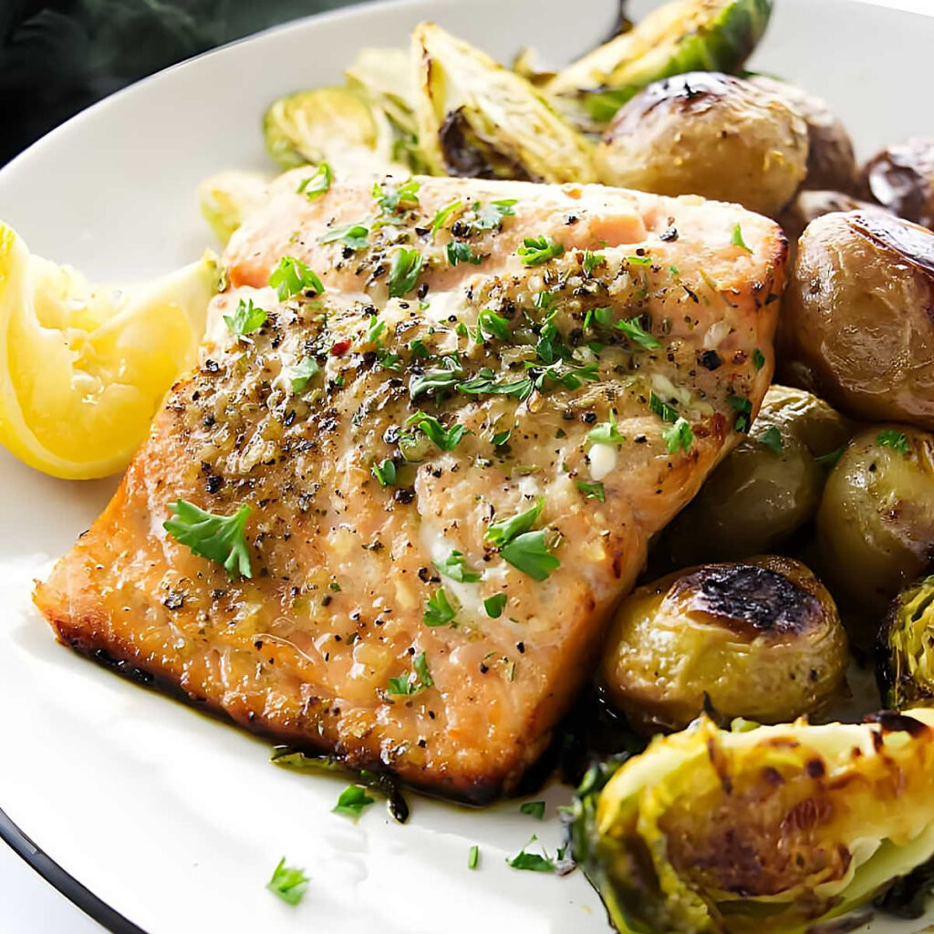 Cooked salmon fillet with baby potatoes, Brussels sprouts, and lemon wedges.
