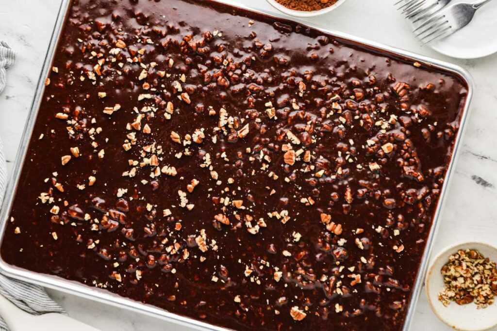 A sheet pan filled with a warm chocolate sheet cake next to a plate and forks.
