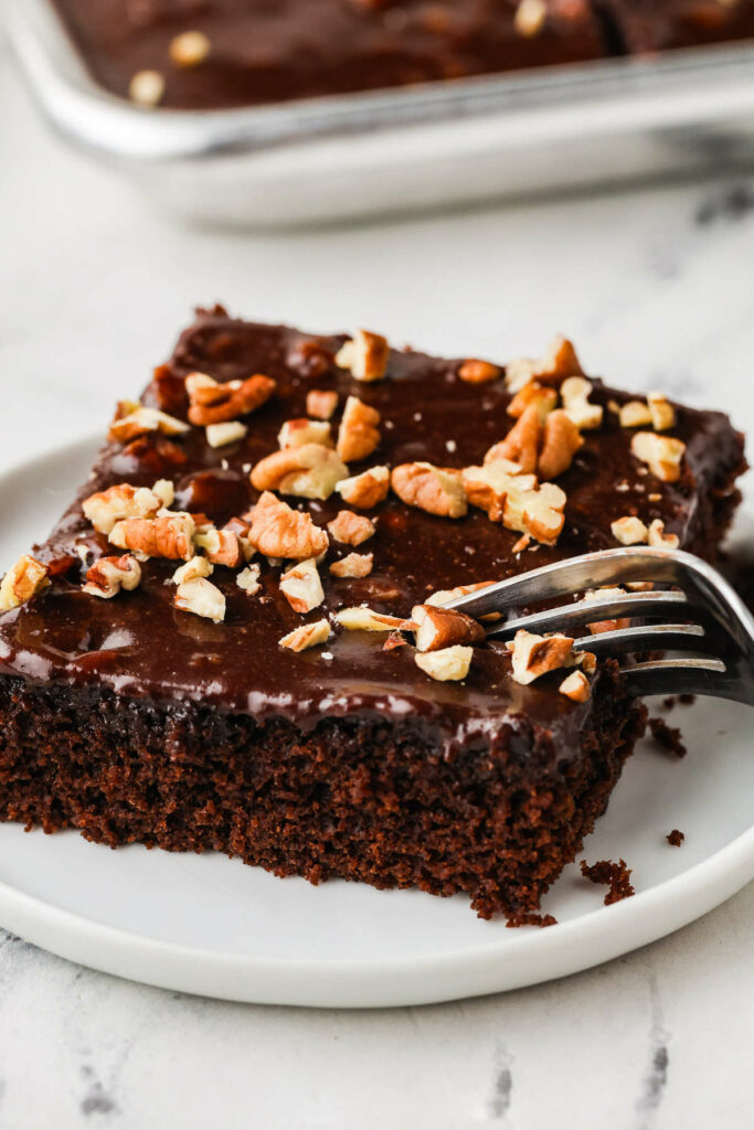 A fork taking a bite from a slice of chocolate sheet cake.