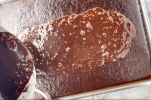 Pouring fudge icing over a warm sheet cake.