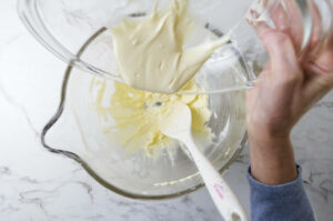 Pouring melted white chocolate into a mixing bowl with butter.